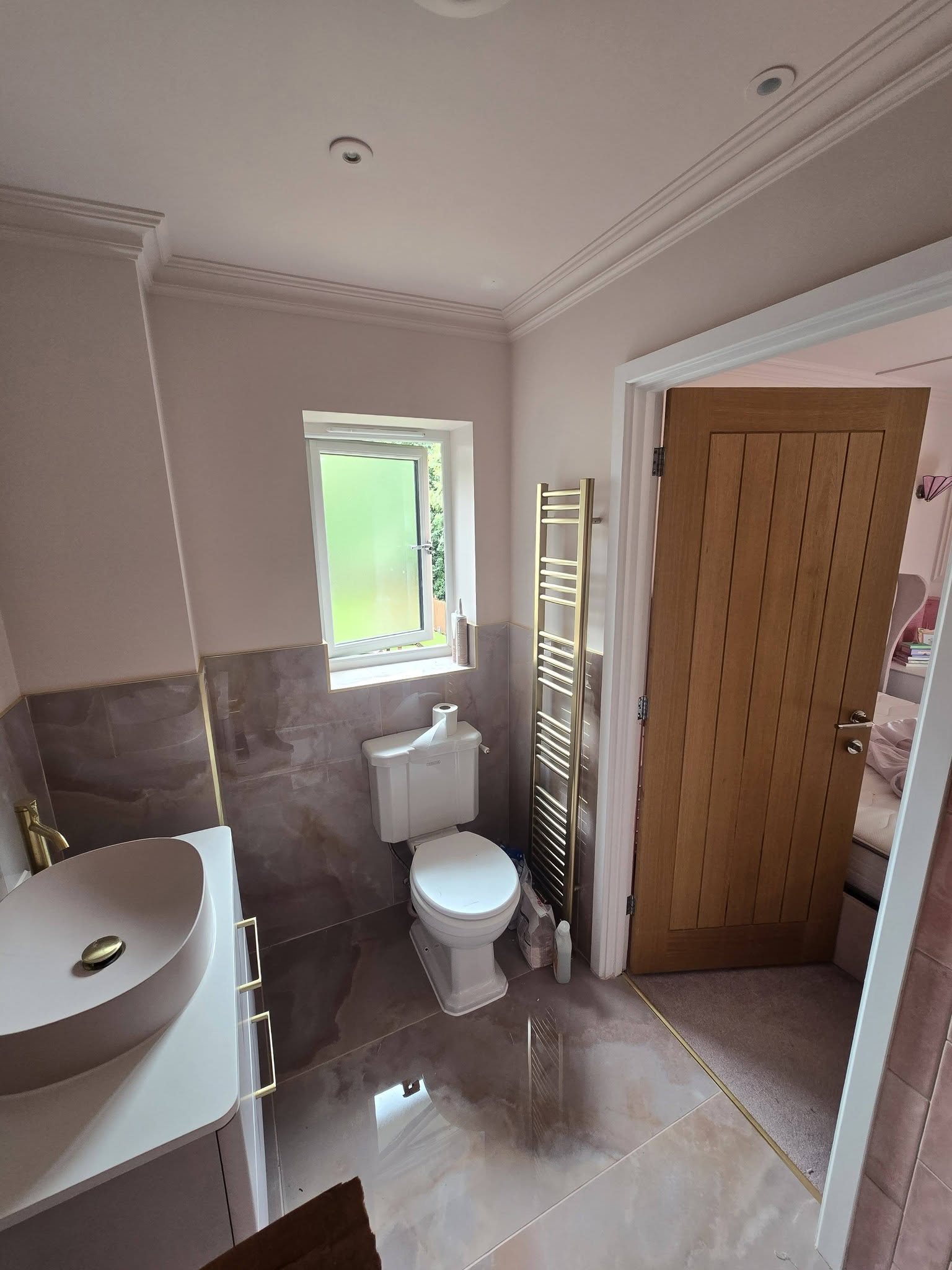 A shower room with a toilet, vanity, gold towel rail and an oak door