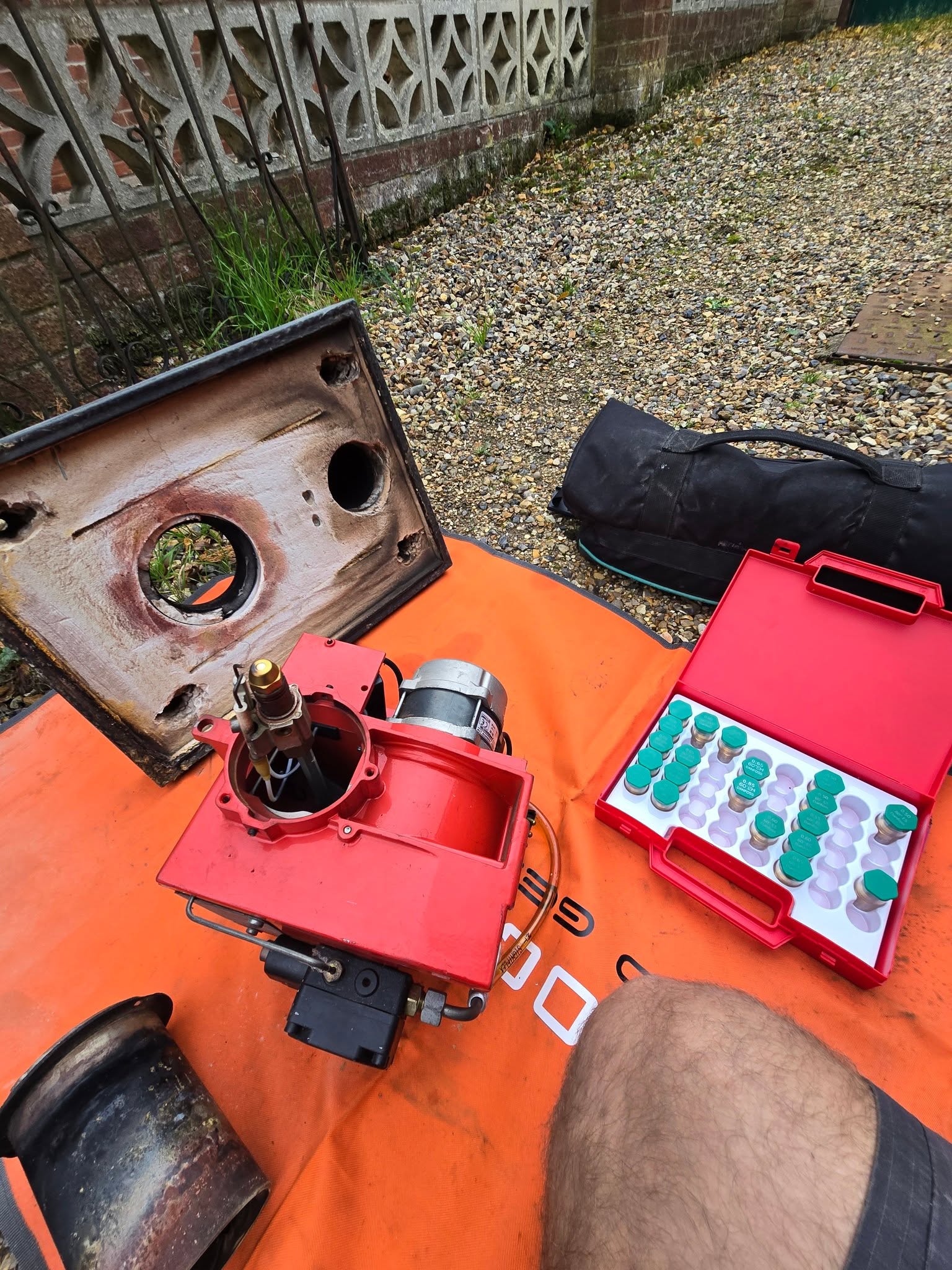 A red boiler burner stripped down on a mat beside a case of parts