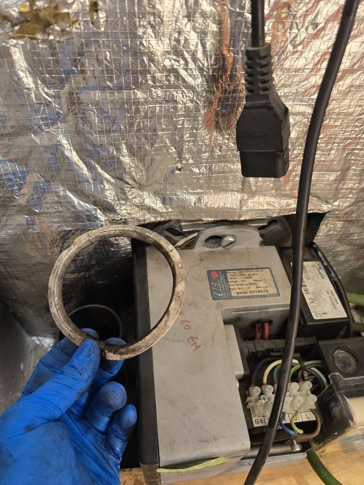 A gloved hand removing a gasket from an opened boiler