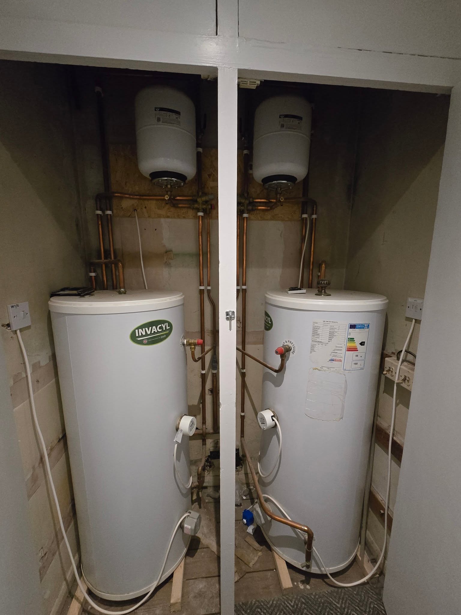 Two hot water cylinders side by side in a cupboard with copper pipework