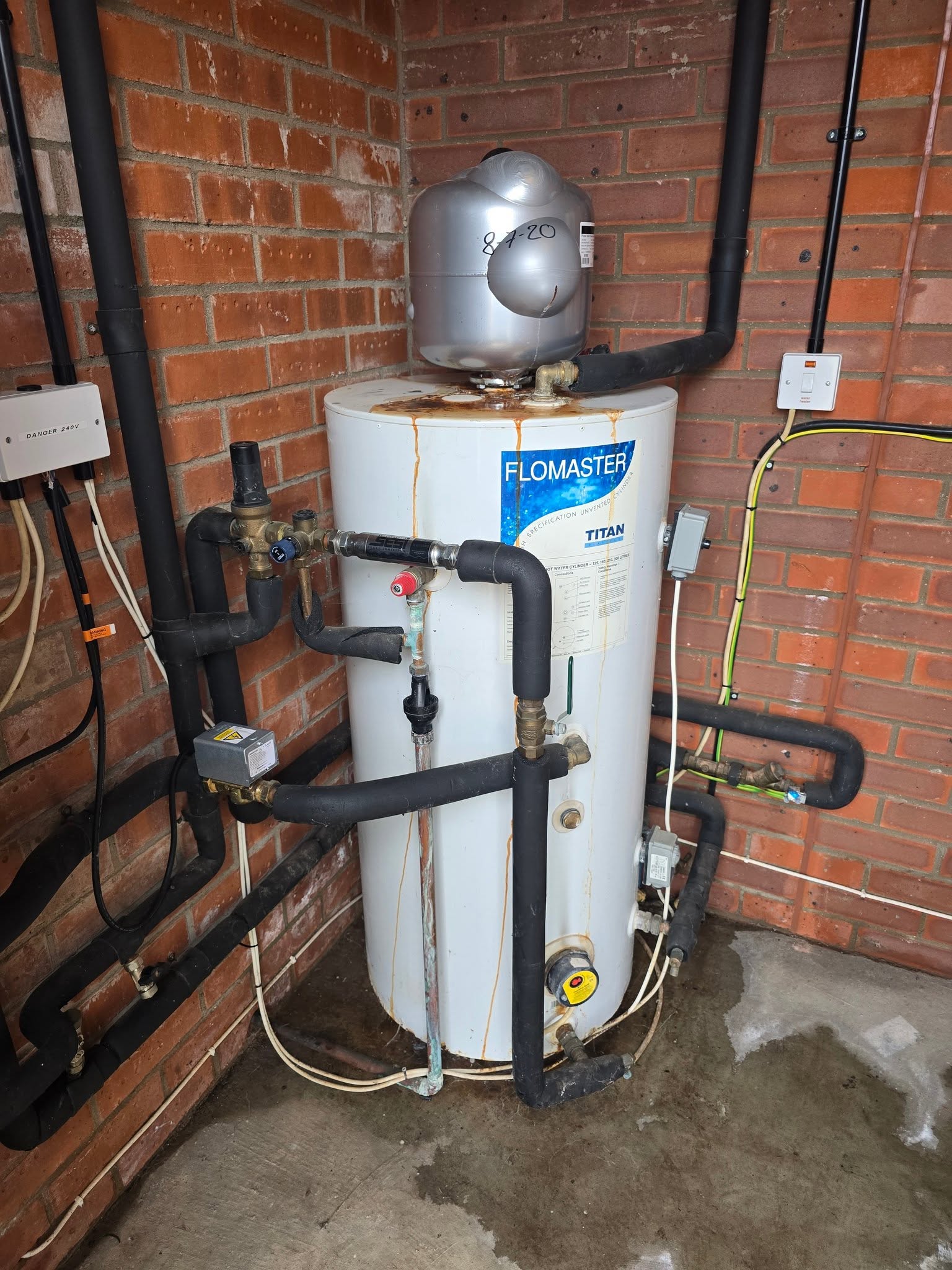 Before: an old Flomaster hot water cylinder in a brick room