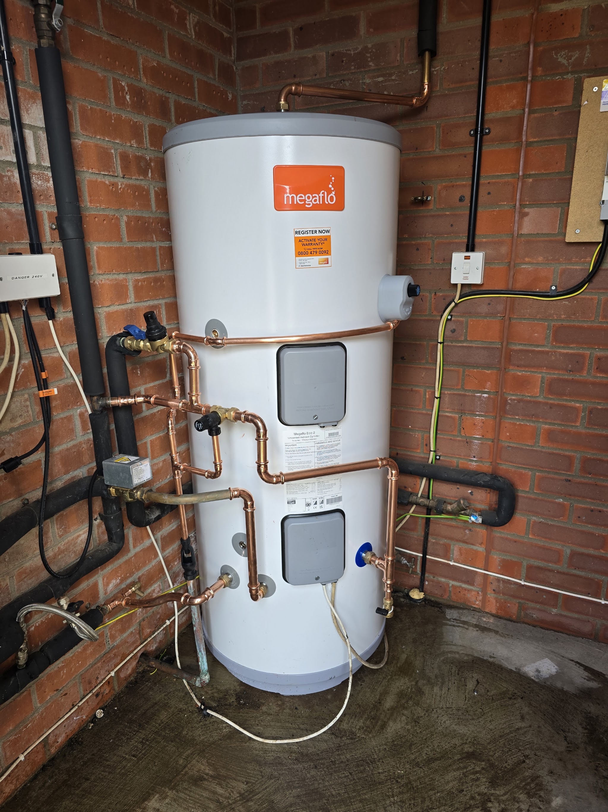 After: a new Megaflo unvented cylinder with copper pipework in the same brick room