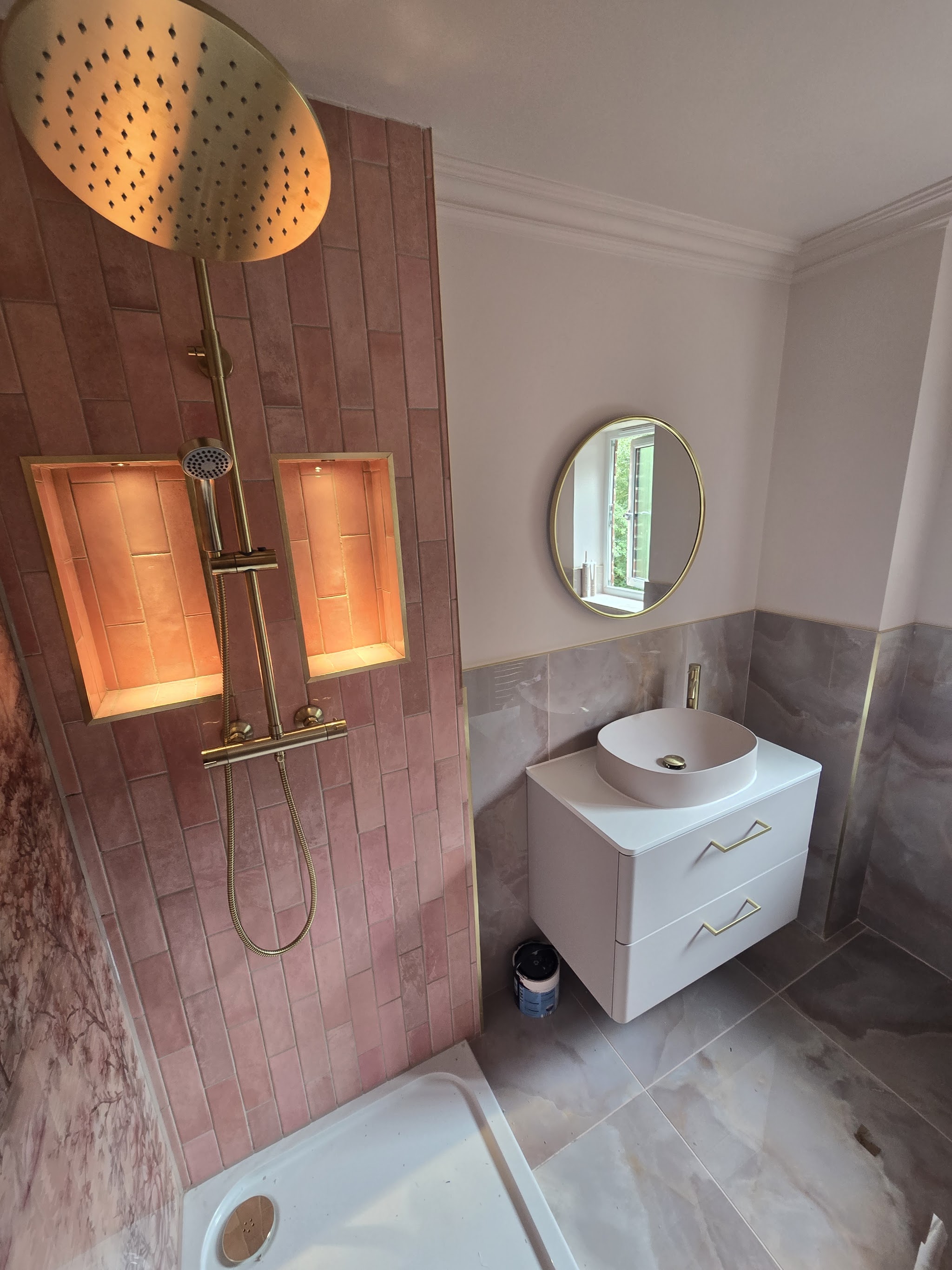 A finished shower room with a gold rainfall shower, lit niches, pink tiles and a floating basin