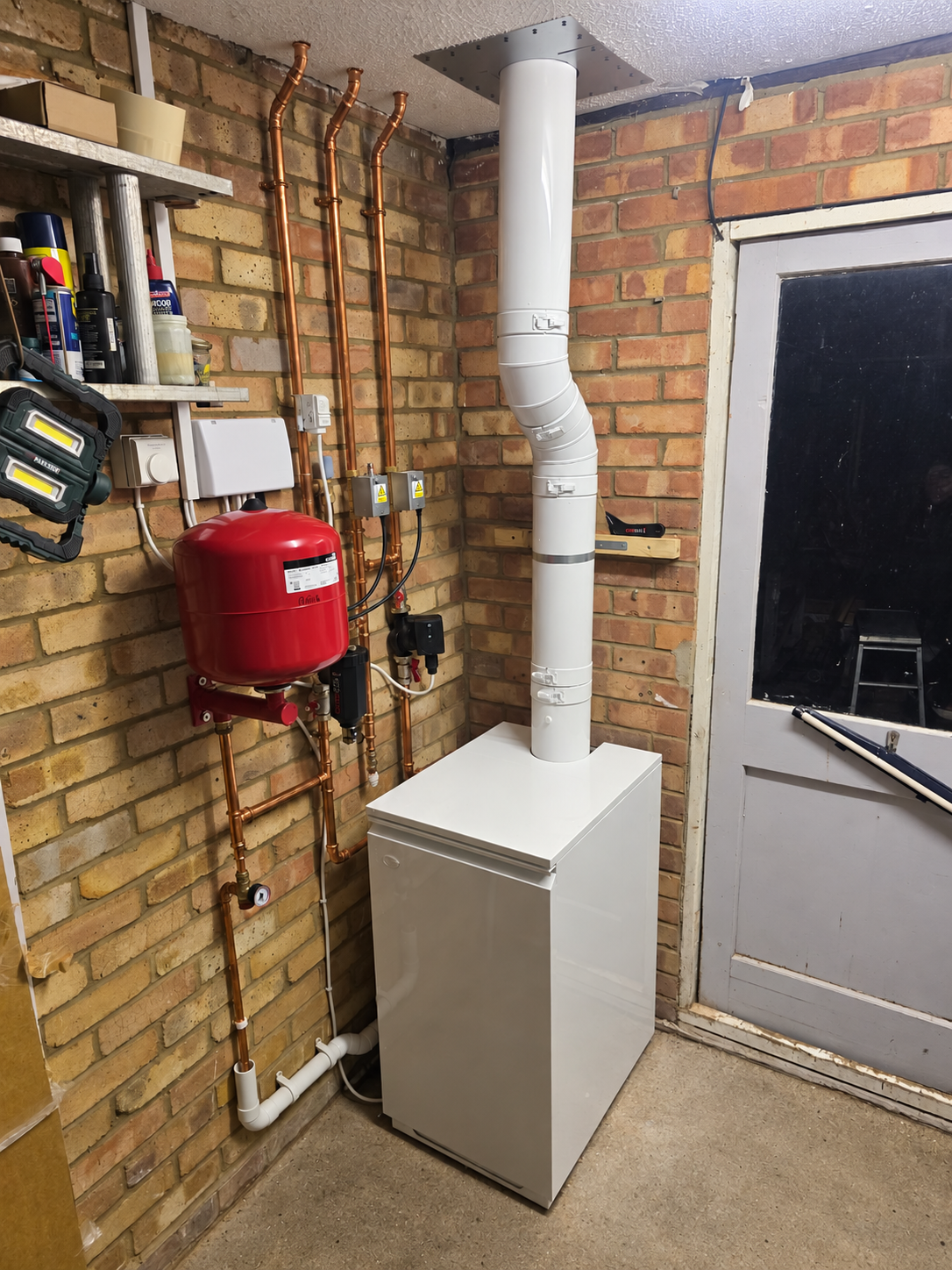 A floor-standing boiler with a flue, red expansion vessel and controls in a utility room