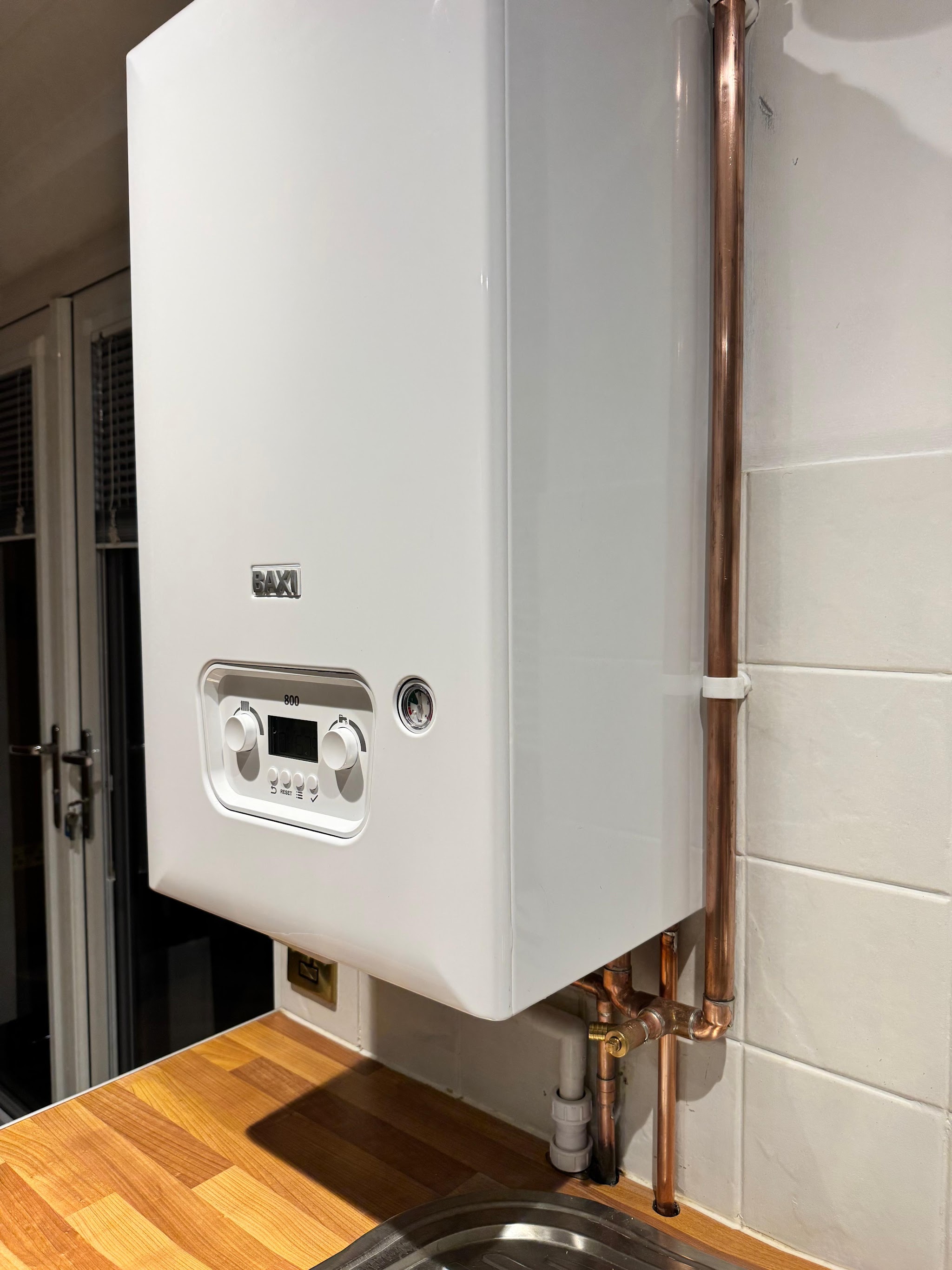 A new Baxi combi boiler on a tiled kitchen wall with neat copper pipework