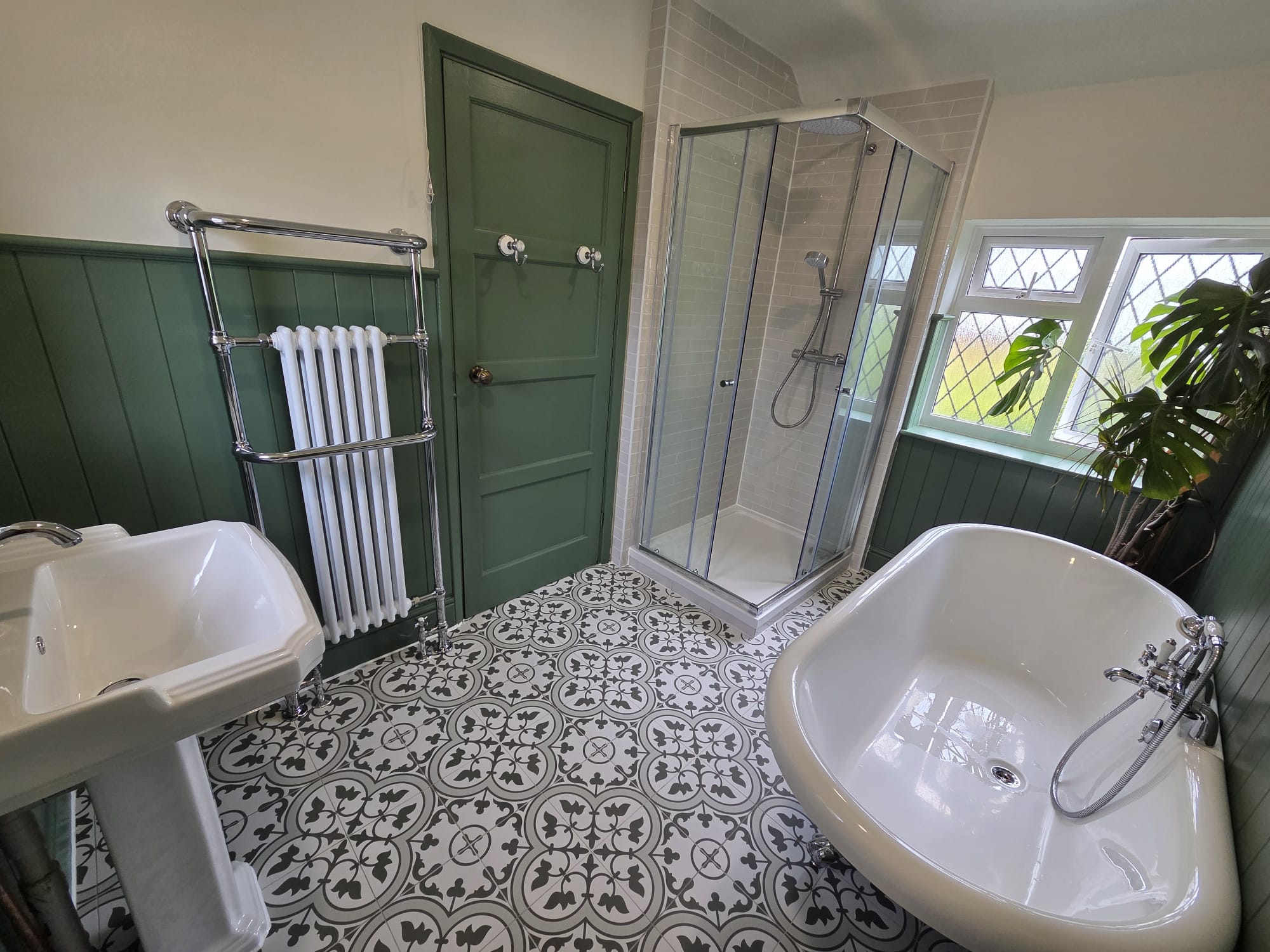 A finished period-style bathroom with a freestanding bath, tall towel radiator, corner shower and patterned floor tiles