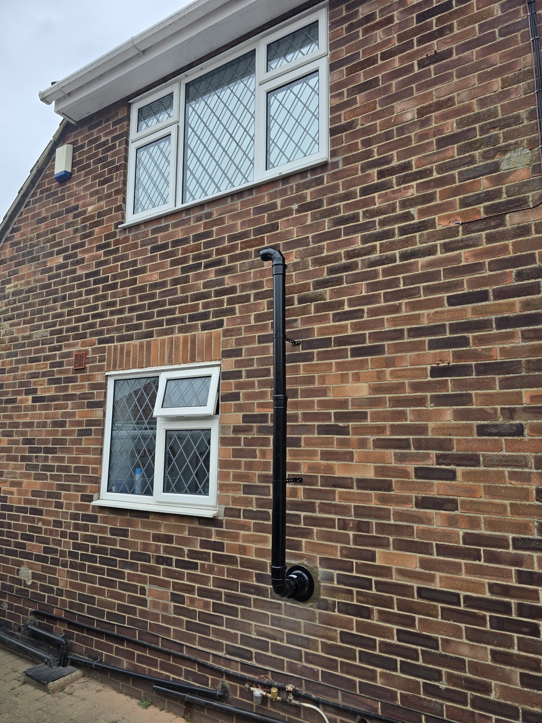 A black flue pipe running up the outside wall of a brick house