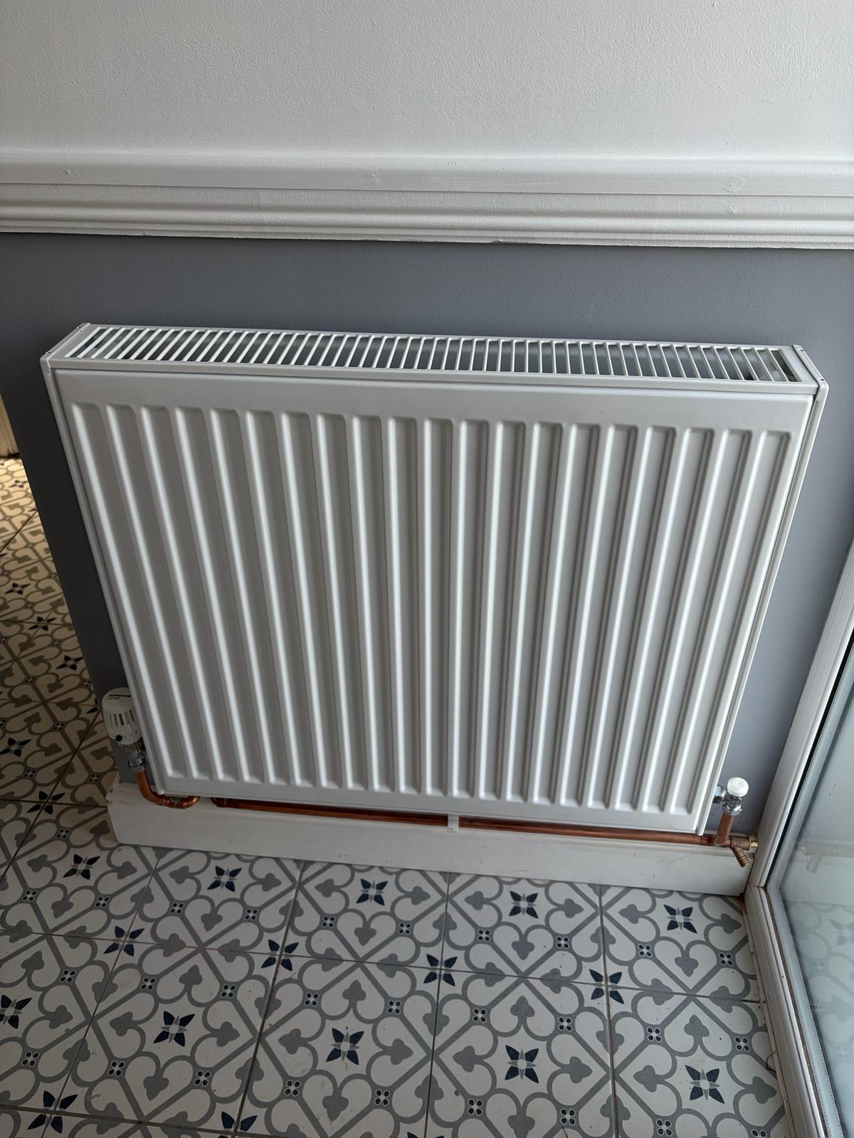 A new white panel radiator above patterned floor tiles